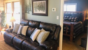 A living room with a leather sofa, a framed forest picture, and a Christmas tree.