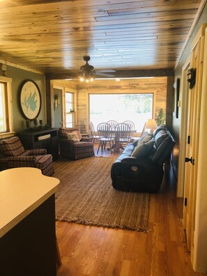 A cozy living room with a wooden ceiling, a large window, and a dining area.