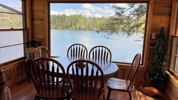 A wooden cabin with a round table and chairs, a view of a lake, and a sign reading "LEECH LAKE".