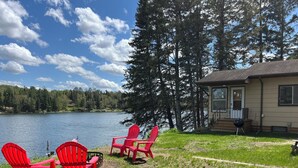 A lakeside property with a house, red Adirondack chairs, and a grill.