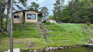A lakeside cabin with a dock, surrounded by trees and a small stream.