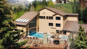 Un bâtiment à deux étages doté d’une grande façade vitrée, d’une piscine et d’une terrasse avec des chaises longues.