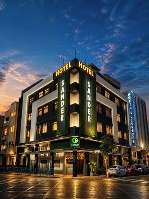 Un hotel con un llamativo letrero que dice 'HOTEL SANDER', una fachada moderna y un cielo despejado al fondo.