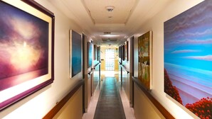 A long, narrow hallway with framed artwork on the walls, leading to a door at the end. - Hotel GH Sander (Guayaquil)