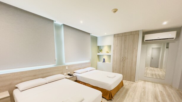 A hotel room with two beds, a wardrobe, a mirror, and an air conditioning unit. - Hotel GH Sander (Guayaquil)