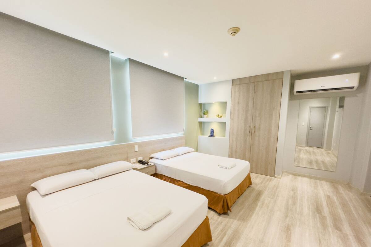 A hotel room with two beds, a wardrobe, a mirror, and an air conditioning unit.