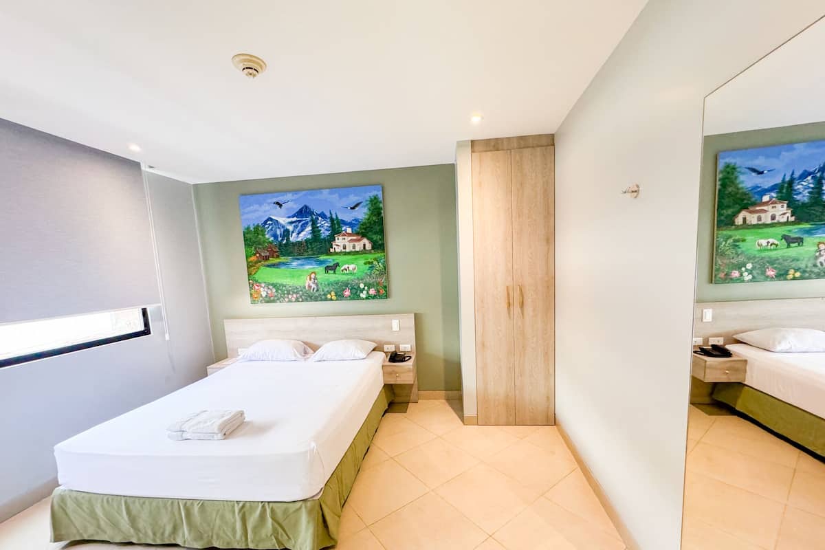 A modern hotel room with a large bed, a painting of a landscape, and a wooden wardrobe.