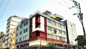 A multi-story hotel with a prominent red and white facade, multiple balconies, and a visible restaurant sign. - Hotel GH Sander (Guayaquil)