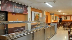 A buffet area with a stainless steel counter and a menu board above it. There are tables and chairs in the background. - Hotel GH Sander (Guayaquil)