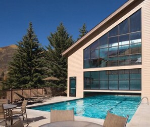A modern building with a swimming pool, outdoor seating, and a view of trees and mountains. - Vibrant 1BR Condo w Gym & Pool Streamside at Vail (Vail)