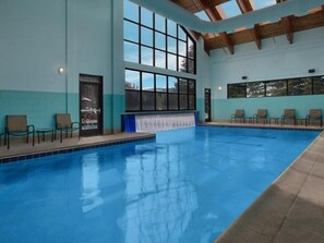 Un'ampia piscina interna con acqua cristallina, circondata da lettini prendisole e grandi finestre.