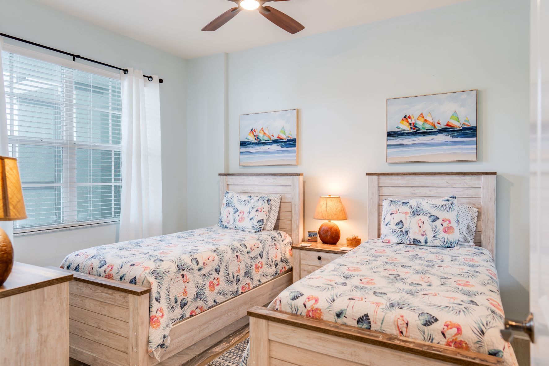 A bedroom with two beds, a ceiling fan, and artwork on the walls.