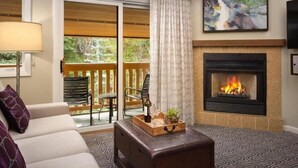 A cozy living room with a fireplace, a sofa, a coffee table, and a balcony with a view of greenery. - Elegant Streamside at Vail Studio with Outdoor Pool (Vail)