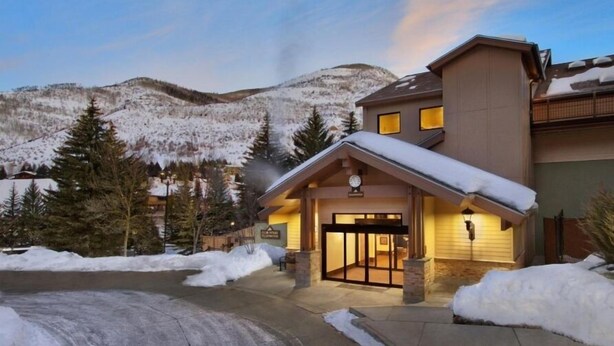 A hotel with a snow-covered entrance, a mountain backdrop, and a well-lit interior. - Elegant Streamside at Vail Studio with Outdoor Pool (Vail)
