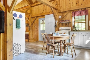 Une cuisine rustique aménagée dans une cabane en bois, avec une table à manger, des chaises, un réfrigérateur, une cuisinière et une fenêtre avec des rideaux.