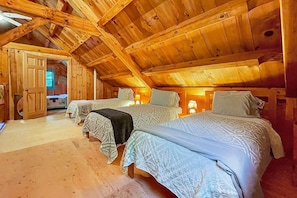Quarto de sótão acolhedor com três camas, vigas de madeira e uma porta que dá para o exterior.