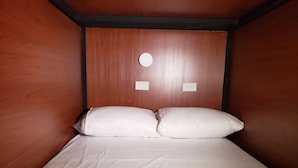 Una cama individual con ropa de cama blanca y dos almohadas en una habitación con paredes de madera y un aplique de luz circular en la pared.