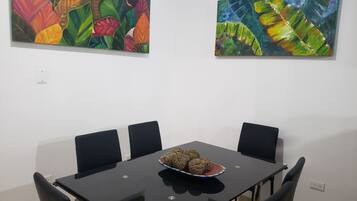 Uma sala de jantar com uma mesa e cadeiras pretas, uma tigela com bolas decorativas e duas pinturas coloridas na parede.