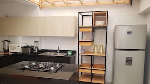 Cocina moderna con una isla central, electrodomésticos de acero inoxidable y una estantería de madera empotrada.