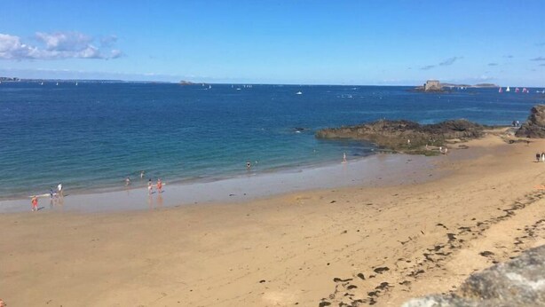A beach with clear blue water, sandy shore, and rocky outcrops.