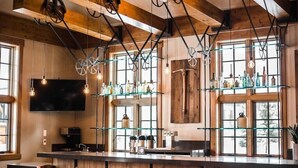 Un espace bar agrémenté de poutres en bois, de luminaires suspendus et d’étagères où sont exposées des bouteilles.