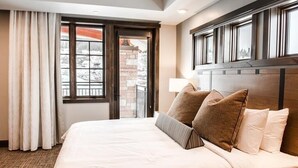 Une chambre d’hôtel avec un grand lit, une vue sur un paysage enneigé par la fenêtre et un mur de briques visible à travers la porte.