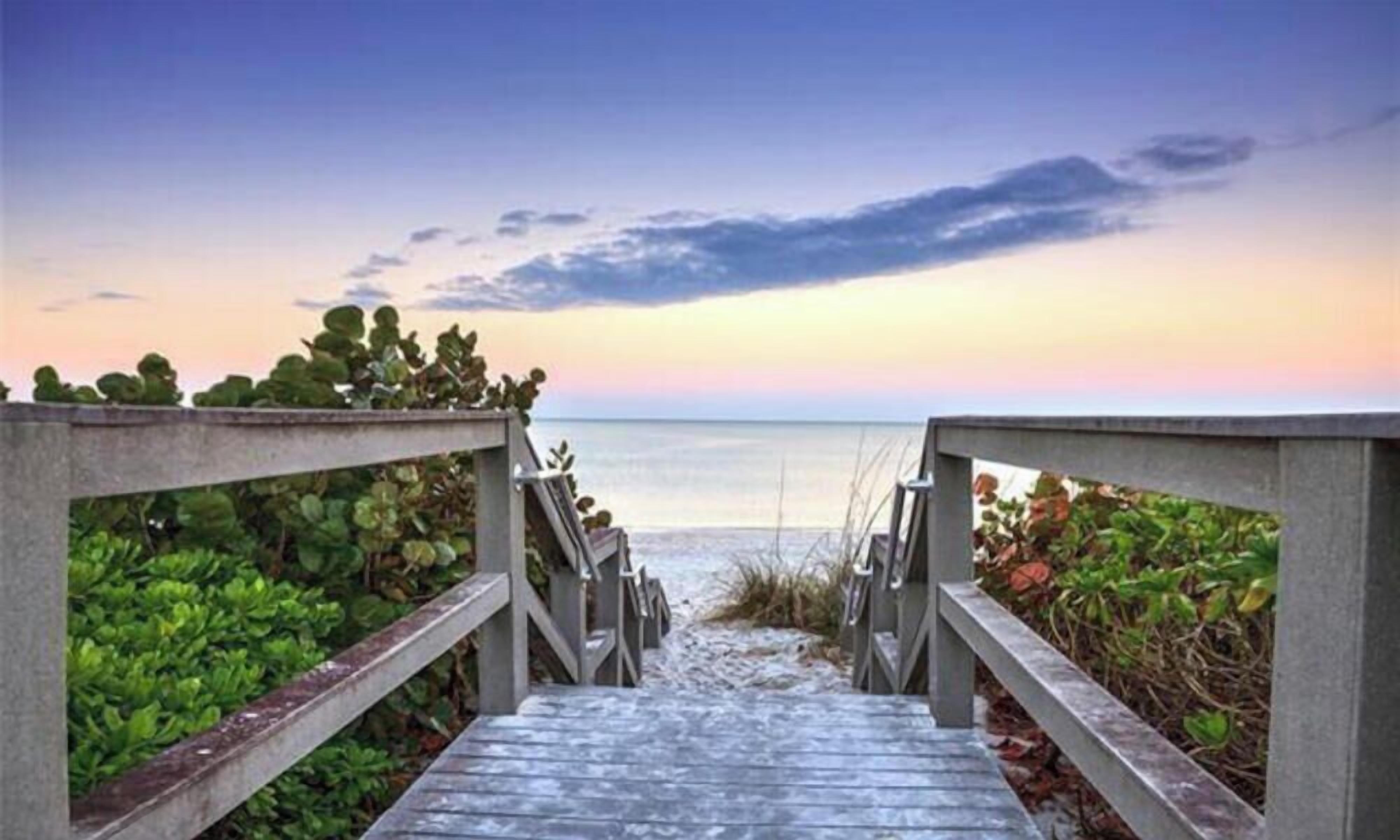 A wooden boardwalk leading to a beach with a concrete railing on both sides.