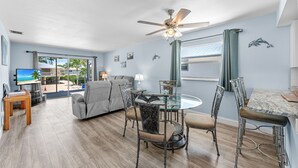 Uma sala de estar espaçosa com uma mesa de jantar de vidro, sofá cinza e um ventilador de teto.