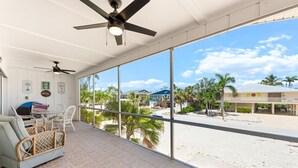 Varanda ampla com vista para a praia, ventilador de teto e sofá de vime.