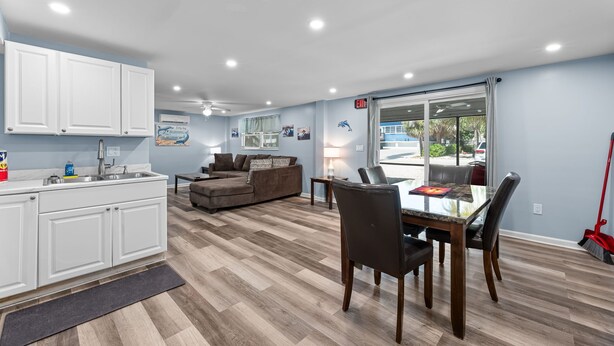 A modern kitchen with white cabinets, a dining area with a glass table, and a living room with a brown sofa.