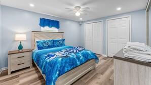 A bedroom with a bed, nightstand, lamp, ceiling fan, and white closets.