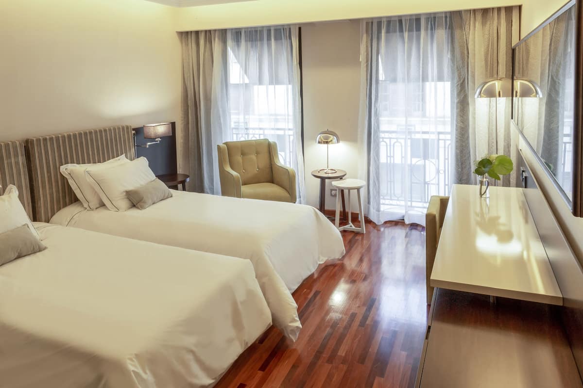 A hotel room with two beds, a desk, a chair, a lamp, and a mirror.