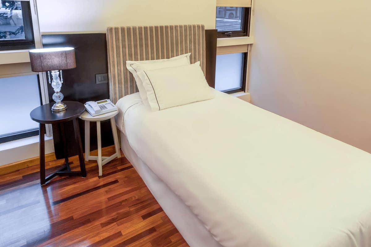 A hotel room with a bed, a bedside lamp, a nightstand, and a window.