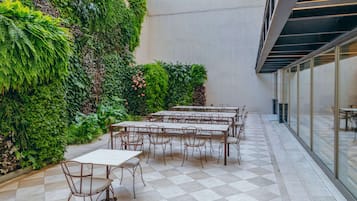 A courtyard with tables and chairs, surrounded by lush greenery and a checkered floor.