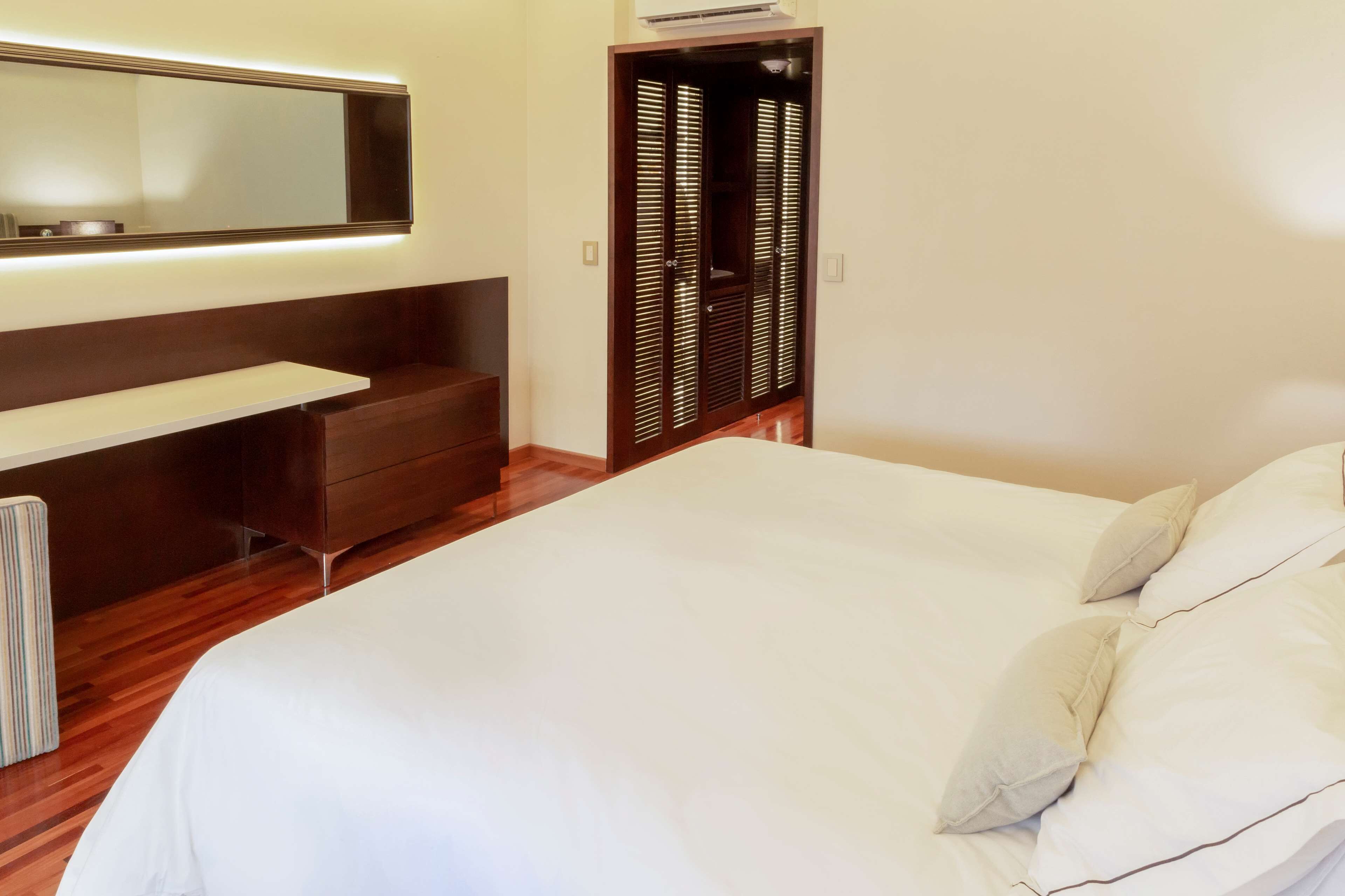 A bedroom with a large bed, a bedside table, a dresser, a wardrobe, and a mirror.