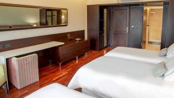A hotel room with two beds, a vanity with a mirror, a wooden floor, and a wardrobe with a door leading to a bathroom.