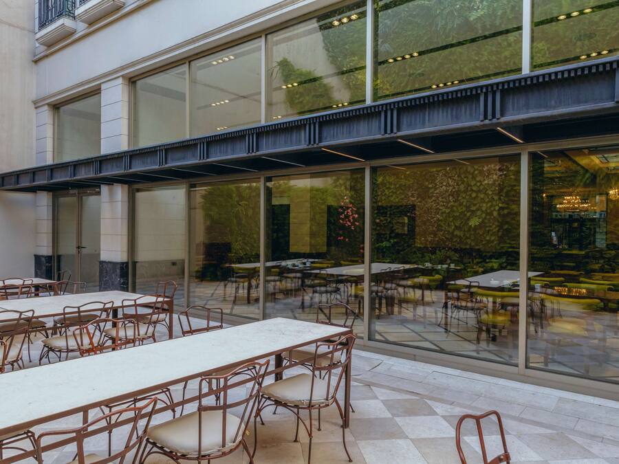 An indoor dining area with tables and chairs, large windows, and a view of the outdoor seating area.