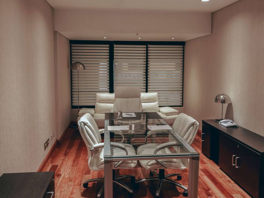 A modern conference room with a glass table, white leather chairs, and a black cabinet.