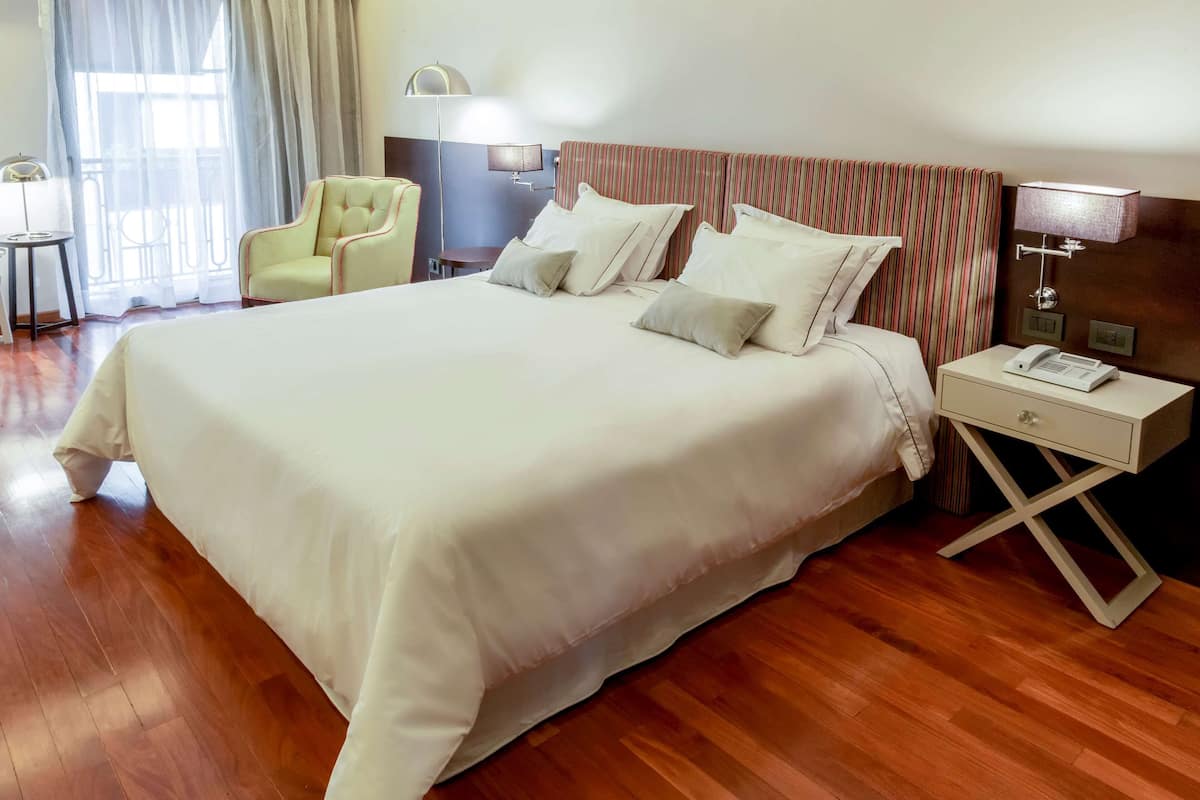 A neatly made bed with white linens, a striped headboard, and a bedside table with a lamp and phone.