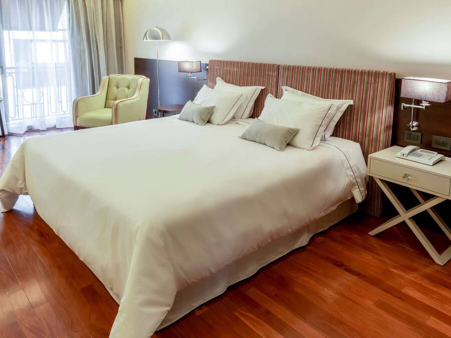 A neatly made bed with white linens, a striped headboard, and a bedside table with a lamp and phone.