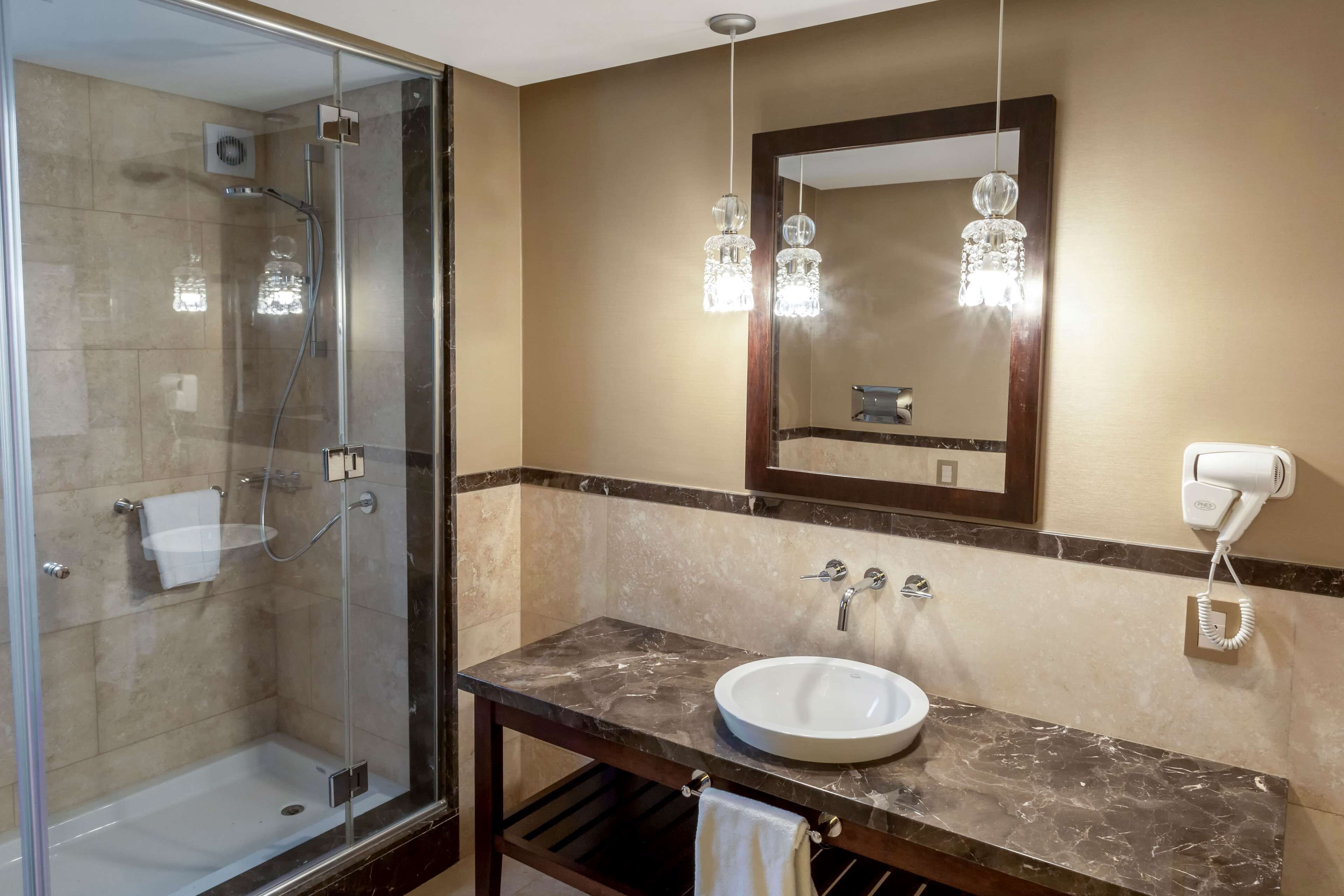 Un bagno con cabina doccia in vetro, lavabo in marmo e luci a sospensione.