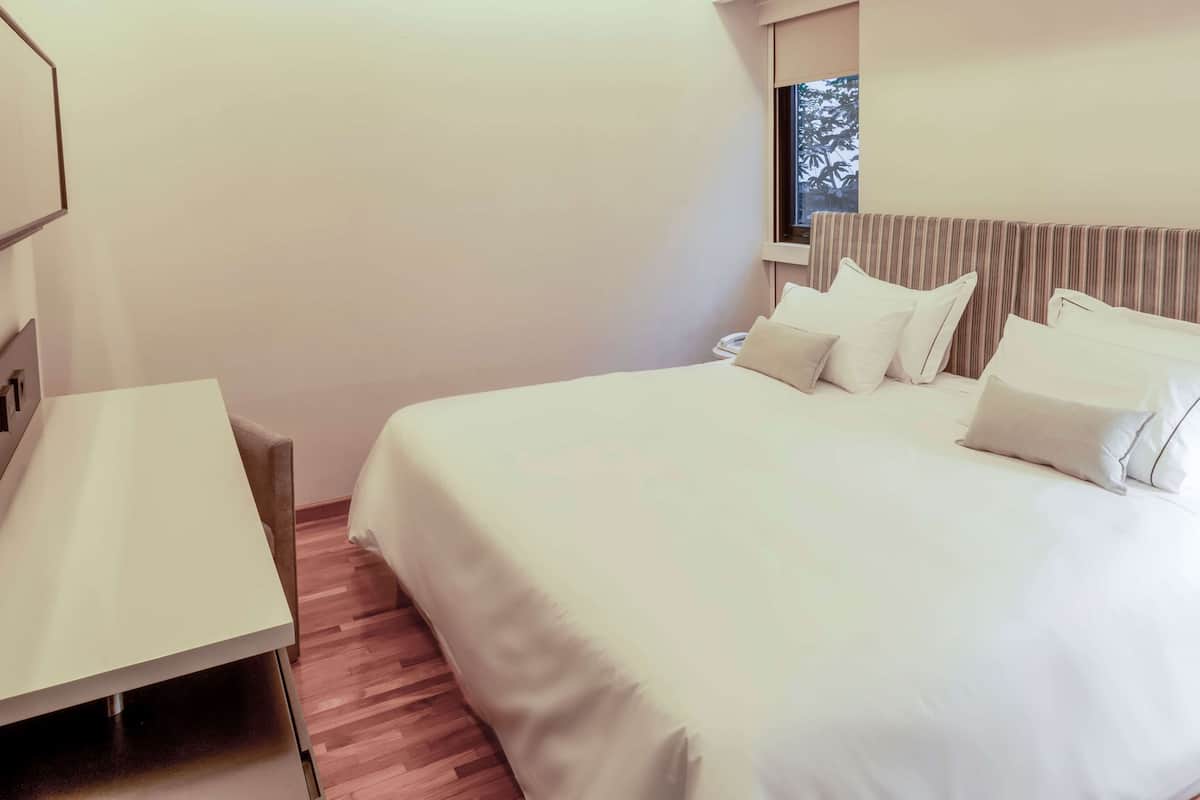 A hotel room with a bed, a bedside table, and a window.