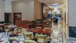 Un vestíbulo de hotel con una recepción, varias áreas de descanso con mesas y sillones, y un candelabro.