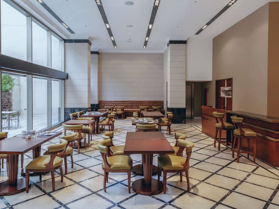 A spacious dining area with multiple tables and chairs, a bar area, and large windows providing natural light.