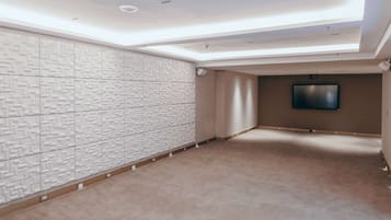 Una habitación amplia y bien iluminada, con un papel tapiz estampado, un televisor de pantalla plana y piso alfombrado.