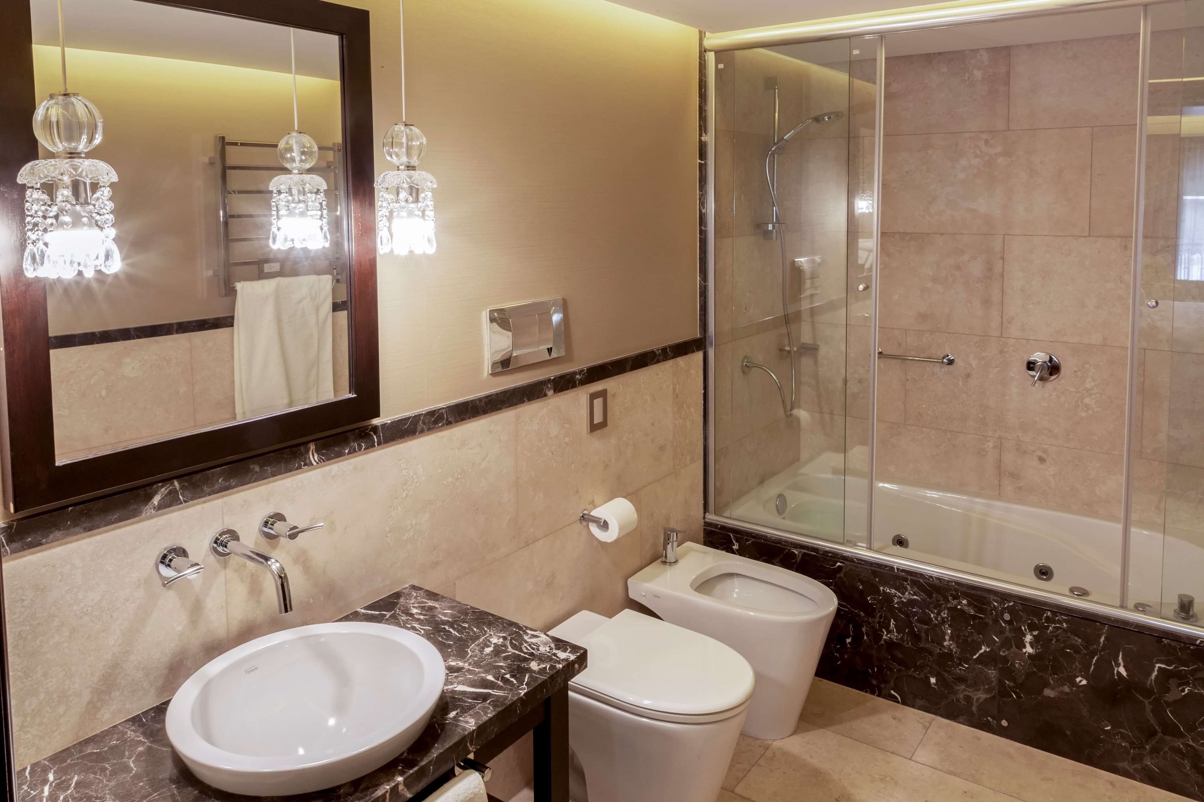 Une salle de bain moderne avec un lavabo en marbre, deux toilettes, une douche à l’italienne et un grand miroir.
