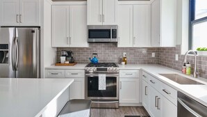 A modern kitchen with white cabinets, stainless steel appliances, and a brick backsplash. - Luxury Rowhome 🏔 Mountain Views Littleton Main St (Littleton)