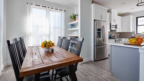 A modern kitchen with white cabinets, a stainless steel refrigerator, and a wooden dining table with chairs. - Luxury Rowhome 🏔 Mountain Views Littleton Main St (Littleton)