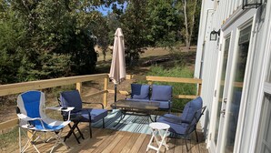 Una terraza de madera con mobiliario exterior, incluyendo una mesa y sillas, y un espacio cubierto con una sombrilla.