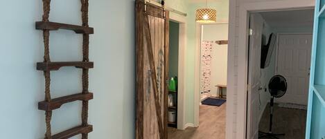 Un couloir avec une échelle en bois, une porte coulissante, un tapis à motifs et un ventilateur.
